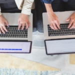 A man and a woman sitting on a bench tipping on an Apple computer