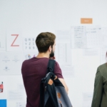 Man and a woman looking at a wall full of papers.